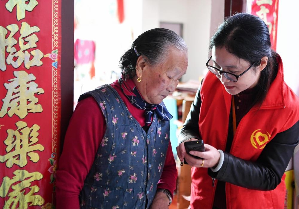 在福州市長樂區(qū)航城街道籌岐村，智慧養(yǎng)老平臺派駐社區(qū)的助老員（右）在為老人陳鳳英（左）講解養(yǎng)老定制手機(jī)的用法（2021年11月26日攝）。新華社記者 魏培全 攝