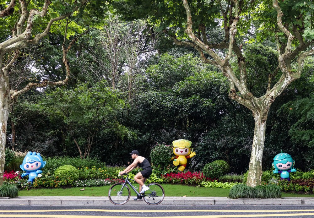 市民在杭州市南山路上一處亞運會主題吉祥物雕塑前騎自行車。
