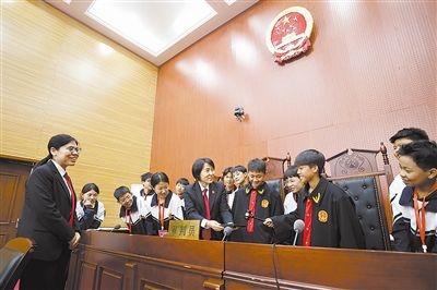 圖③：同學(xué)們穿法袍、敲法槌，爭(zhēng)做“小法官”。