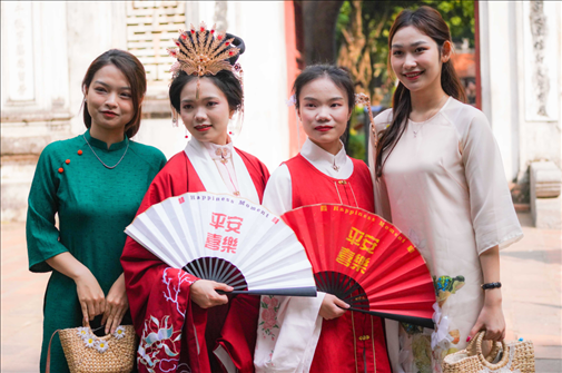 身穿古裝的中國游客和身穿越南傳統(tǒng)服飾奧黛的越南青年在文廟門前合影。