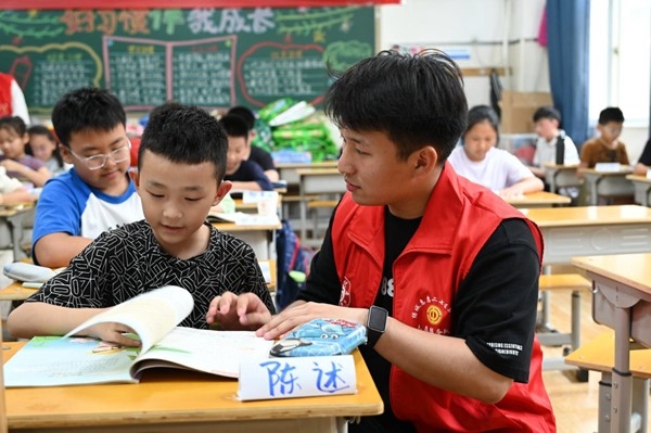 鄭州市二七區(qū)暑托班的志愿者輔導(dǎo)孩子寫作業(yè)。人民網(wǎng)記者王玉興攝